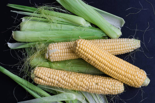 Rijpe maïs en graan op een zwarte achtergrond, bovenaanzicht, ruimte voor kopiëren - Foto, afbeelding