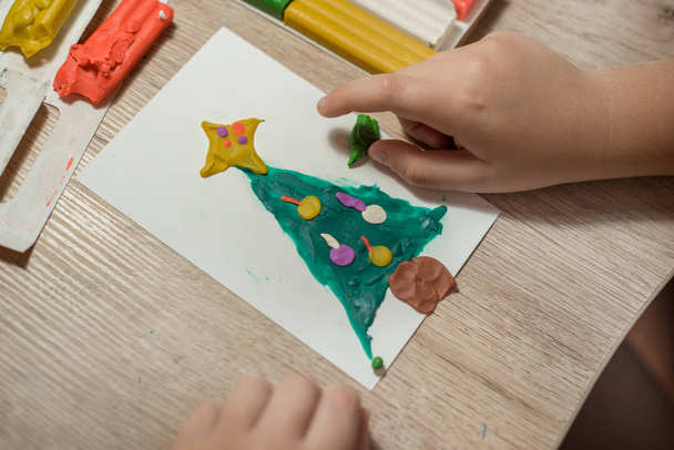 Christmas children's craft of plasticine. a green Christmas tree with balls and toys. The concept of a New Year's holiday with gifts - Zdjęcie, obraz