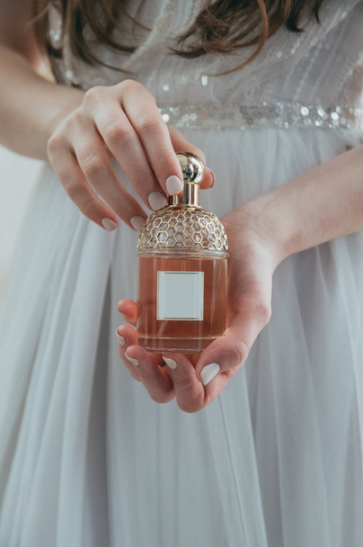 Beyaz elbiseli bir kız bir şişe parfüm ile tutar - Fotoğraf, Görsel