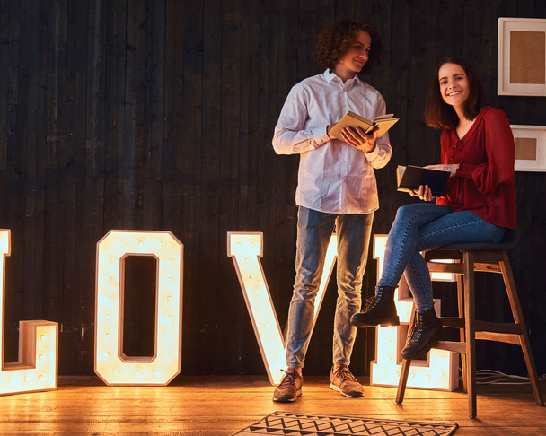 Jovem casal estudante lendo juntos em uma sala decorada com letras volumosas com iluminação
. - Foto, Imagem