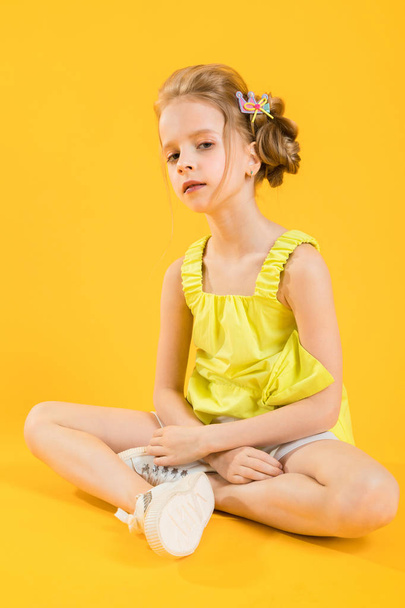 A teenage girl is sitting on a yellow background. - Foto, Imagem
