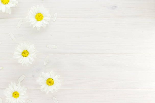 Witte madeliefjes en tuin bloemen op een wit houten tafel. De bloemen zijn gerangschikt kant, lege ruimte gelaten aan de andere kant. - Foto, afbeelding