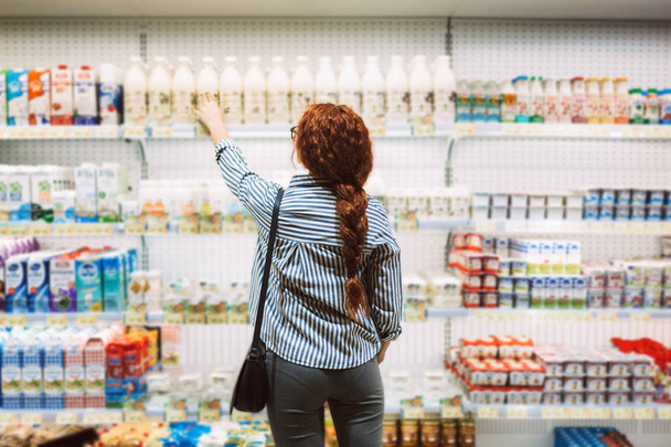 Süt ve süt ürünleri modern süpermarkette seçme arkadan çizgili gömlekli genç kadın - Fotoğraf, Görsel