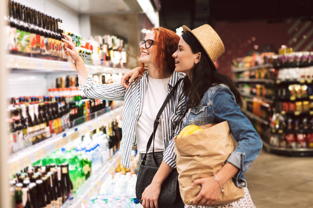 Ładne dziewczyny z papier spożywczy torbą pełną produktów radośnie wybór produktów w nowoczesny supermarket - Zdjęcie, obraz