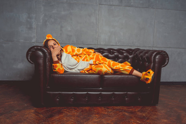 Pajamas in the form of a giraffe. Emotional portrait of a student on the background leather sofa. Crazy and funny man in the suit. - Foto, immagini