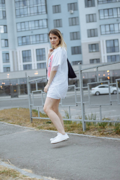 Beautiful woman with nude legs walking around city street wearing long white shirt and jacket - Photo, Image