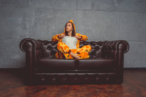 Pajamas in the form of a giraffe. Emotional portrait of a student on the background leather sofa. Crazy and funny man in the suit. - Foto, Imagen