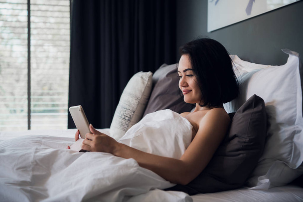 ベッドに座って、デジタル タブレットを使用して、笑って幸せの若い白人女性の肖像画 - 写真・画像