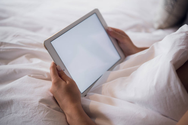 atractiva chica morena sosteniendo tableta digital con pantalla en blanco y sonriendo en el dormitorio
 - Foto, imagen