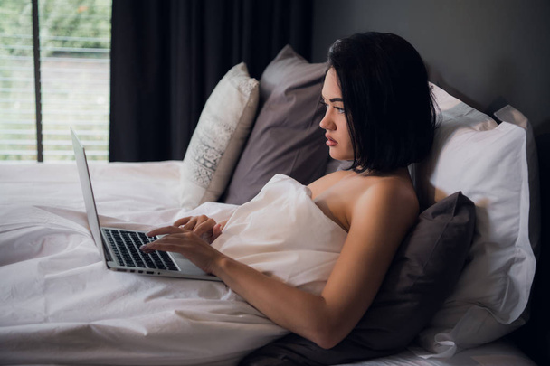 Portrait of beautiful young woman with laptop on bed - 写真・画像