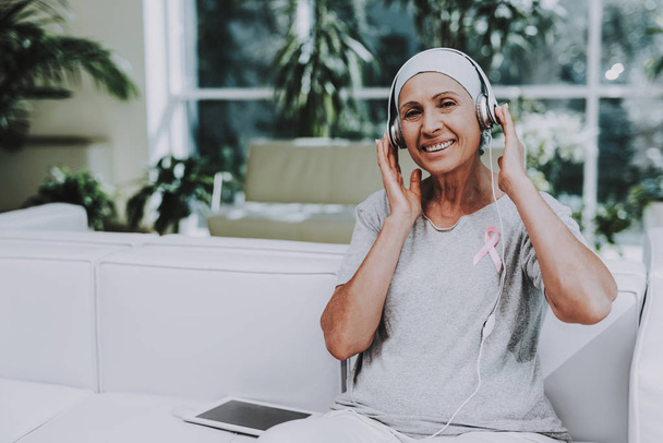 Patient Undergoes Rehabilitation. Cancer Patient on Sofa. Recovering Woman. Remission. Clinic. Cancer Patient. Flowerpots with Flowers. Pink Ribbon. Breast Cancer. Music on Tablet. White Headphones. - Foto, Imagem