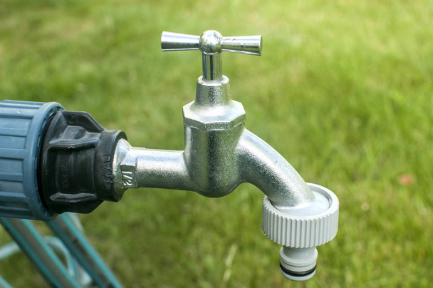 Water tap with plastic garden hose adapter closeup on garden green grass background - Photo, image