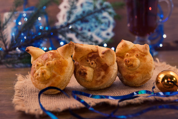 Three baked heads of puff pastry piglets-the edible symbol of 201 next to Christmas decorations and toys. - Photo, Image