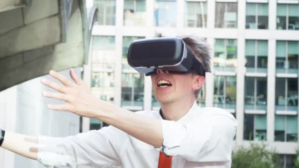 Middle aged caucasian businessman wearing Virtual Reality goggles outside the office playing immersive 360 video game - 映像、動画