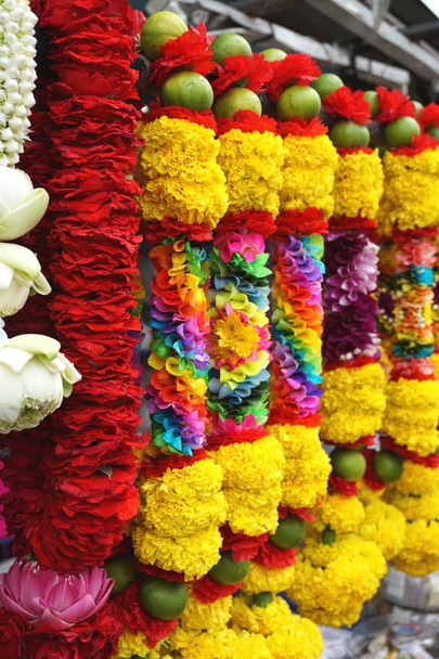 guirlandas coloridas em um arco-íris de cores, incluindo vermelho e amarelo, arco-íris e frutas verdes. Venda em um mercado ao ar livre perto de um templo hindu em Bangkok Tailândia. Os devotos lhes darão como oferendas durante as orações
. - Foto, Imagem