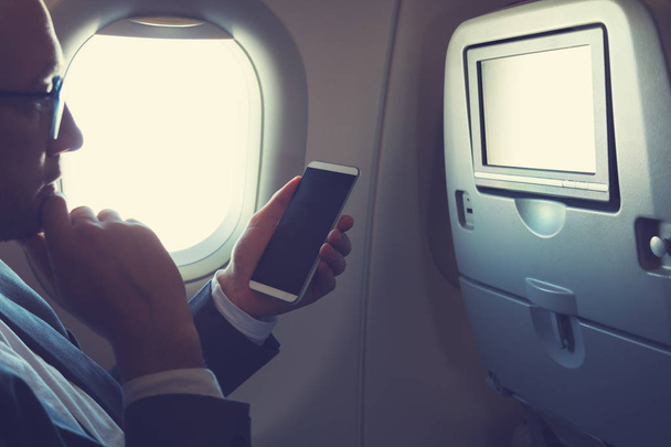 Uçağın içinde Smartphone kullanarak ve düşünce pencereden bakarak adam. - Fotoğraf, Görsel