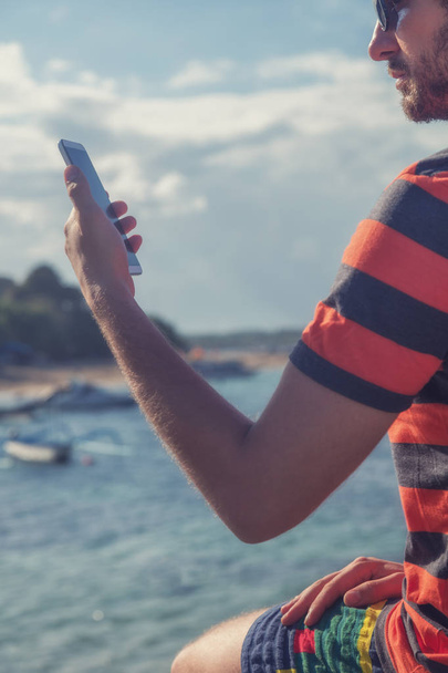 Nuori mies käyttää matkapuhelinta / älypuhelinta lähellä merta
. - Valokuva, kuva