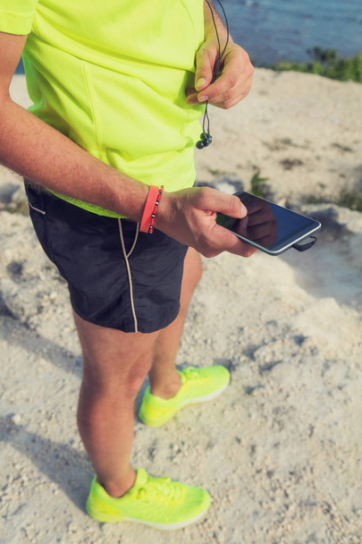 Jogger / runner holding a cellphone with earbuds outdoors. - Photo, image
