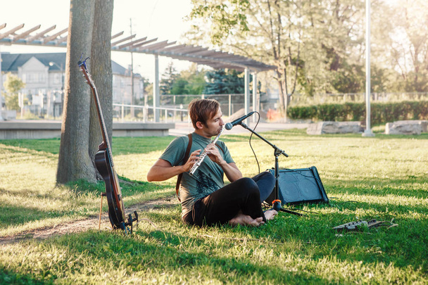 Portrait du musicien blanc caucasien jouant de la flûte dans le parc à l'extérieur au coucher du soleil d'été. Homme jouant de la musique comme une activité de loisir. Performance en direct à l'extérieur
. - Photo, image