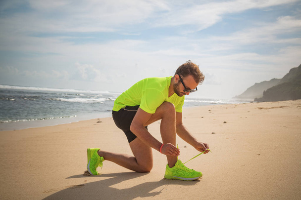 Tying jogging / running shoes on a tropical sandy beach near sea / ocean. - Фото, изображение