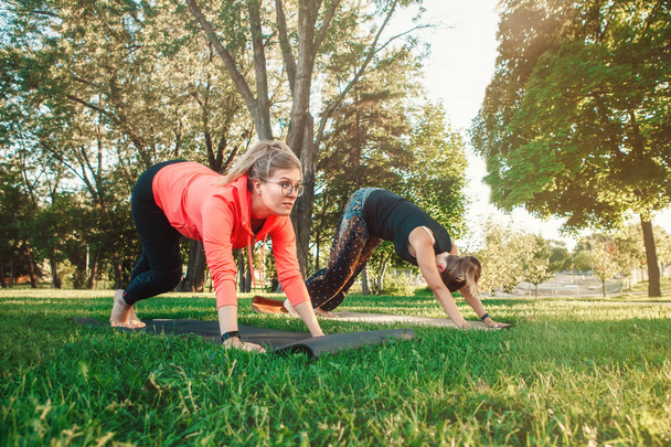 Dwóch osób rasy kaukaskiej robi joga w parku na zewnątrz na zachód słońca. Kobiety, rozciąganie, wykonywanie treningu na świeżym powietrzu. Zdrowy tryb życia współczesnego sportu aktywności.  - Zdjęcie, obraz