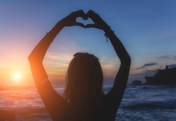 Dziewczyna trzyma kształt serca nad oceanem / brzeg morza. - Zdjęcie, obraz