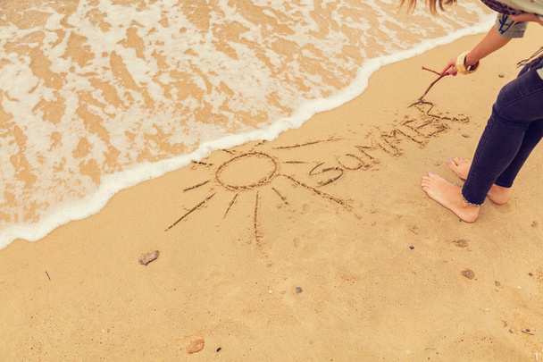 Girl drawing a sun in the sand of ocean / sea beach. - Photo, Image