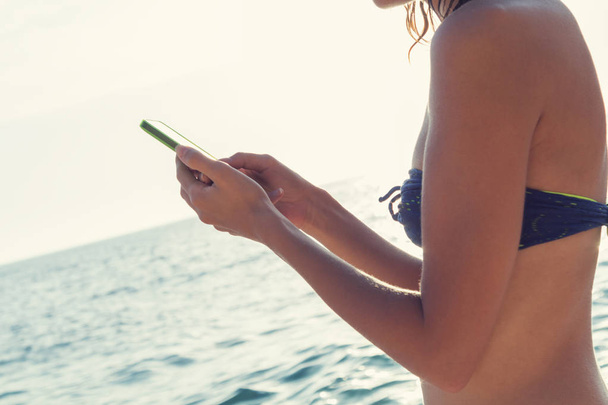 Młoda dziewczyna przy użyciu telefonu komórkowego w pobliżu morza / ocean. - Zdjęcie, obraz