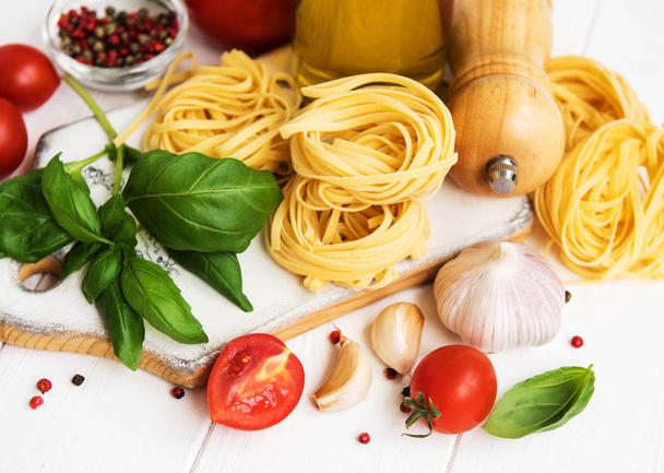 Zutaten italienischer Küche, Olivenöl, Gewürze, Pasta und Tomaten auf einem weißen Holztisch - Foto, Bild