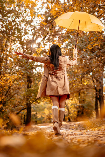 Young woman with yellow umbrella walking in sunny autumn park - Фото, зображення