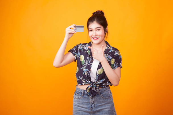 Young Asian woman point to a blank card in  tropical shirt on yellow background - Fotó, kép