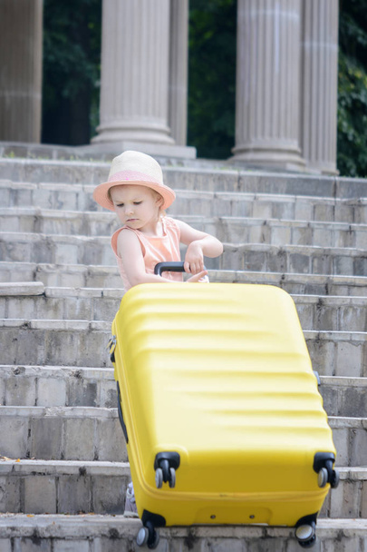 Милая маленькая девочка с большим желтым чемоданом на улице
 - Фото, изображение