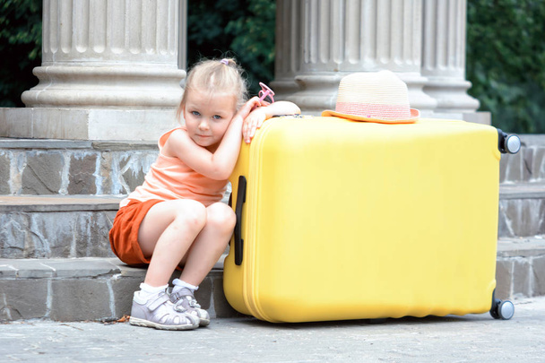Schattig klein meisje met grote gele koffer buitenshuis - Foto, afbeelding