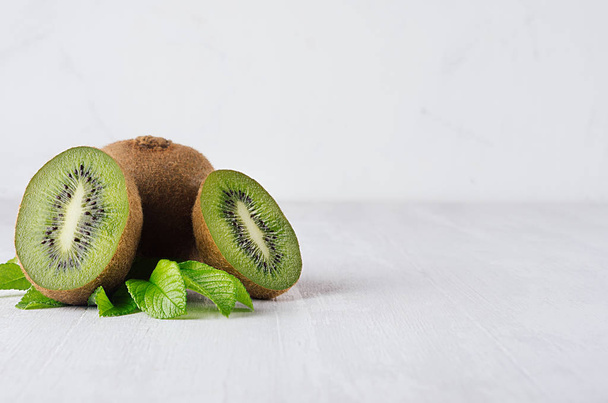 Juicy fresh kiwi with slice, leaves closeup on white wooden background, copy space. Elegance light soft fruits backdrop. - 写真・画像