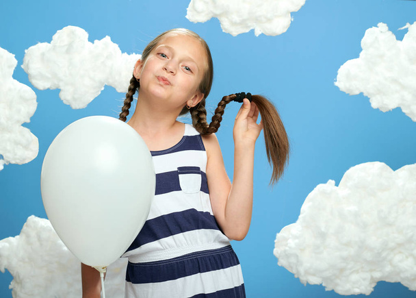Dziewczyna ubrana w paski sukienkę pozowanie na niebieskim tle z bawełny chmury, biały balon, koncepcja lato i szczęścia - Zdjęcie, obraz