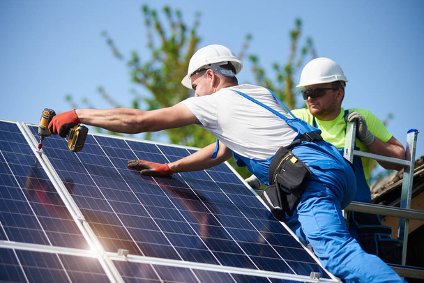 Twee werknemers technici zware zonne-foto-voltaïsche panelen verbinden met hoge stalen platform. Exterieur zonnestelsel installatie, alternatieve hernieuwbare groene energie generatie concept. - Foto, afbeelding