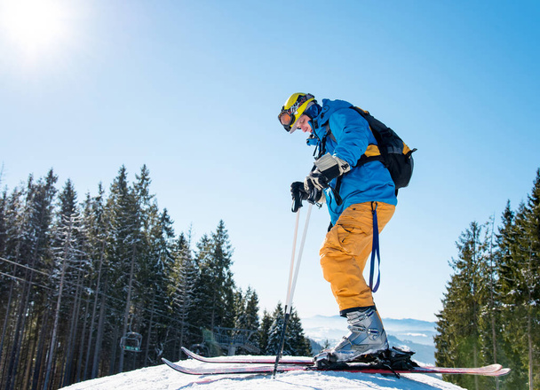 Χαμηλή γωνία πυροβολισμό ενός άνδρα σκι στα βουνά, φορώντας τα σκι, απολαμβάνοντας ηλιόλουστη χειμωνιάτικη ημέρα σε εξωτερικούς χώρους. Χειμερινό θέρετρο - Φωτογραφία, εικόνα