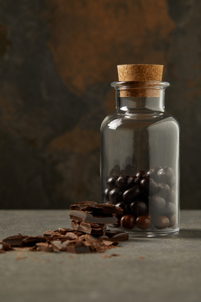 close-up view of chocolate pieces and gourmet chocolate balls in glass jar on grey - Foto, afbeelding