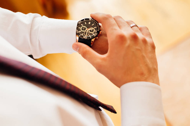 Detailní stylové hodinky na ženichově ruce, který se dívá na číselník - Fotografie, Obrázek