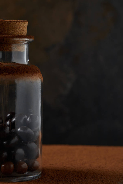 vergrote weergave van gastronomische chocolade ballen in glazen pot en cacao poeder op donkere achtergrond - Foto, afbeelding