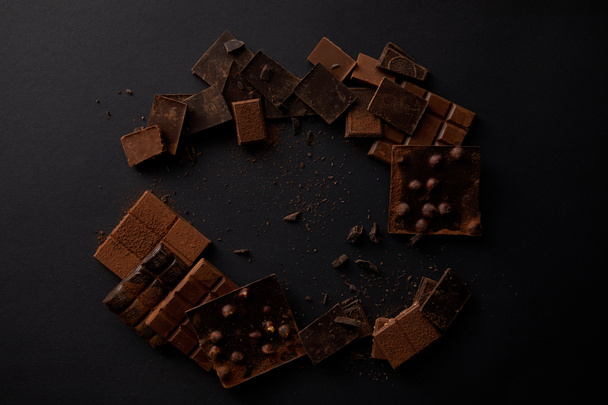 top view of assorted gourmet chocolate pieces on black background   - Фото, зображення