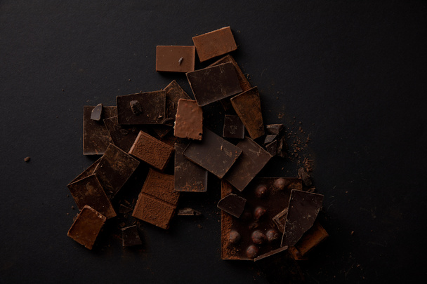 top view of gourmet chocolate pieces with hazelnuts on black - Fotó, kép