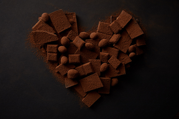 top view of tasty chocolate with nuts and cocoa powder arranged in shape of heart on black - Foto, imagen