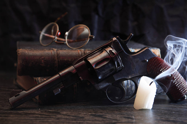 Натюрморт со старым револьвером рядом с книгой и погасшей свечой
 - Фото, изображение