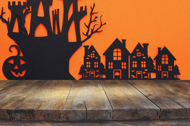 Concepto de Halloween. Mesa rústica vacía frente al pueblo embrujado sobre fondo naranja. Listo para montaje en pantalla de producto
 - Foto, Imagen