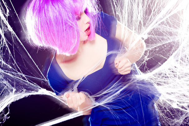 mujer sexy con peluca púrpura y maquillaje intenso atrapado en una tela de araña gritando- rodaje de moda
 - Foto, Imagen
