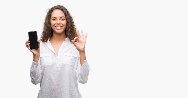 Young hispanic woman using smartphone doing ok sign with fingers, excellent symbol - Foto, Bild