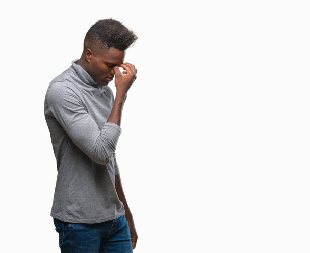 Jonge Afro-Amerikaanse man over geïsoleerde achtergrond moe wrijven neus en ogen, vermoeidheid en hoofdpijn gevoel. Stress en frustratie concept. - Foto, afbeelding
