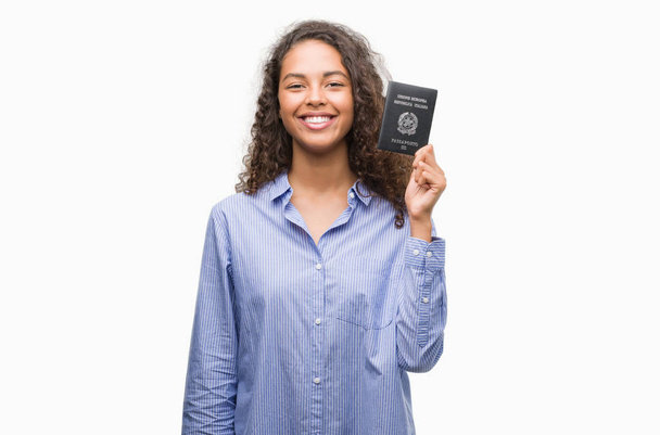 Jeune femme hispanique tenant passeport de l'Italie avec un visage heureux debout et souriant avec un sourire confiant montrant les dents
 - Photo, image