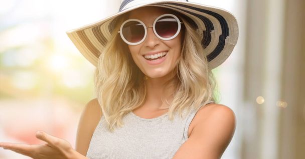 Young woman wearing sunglasses and summer hat holding something in empty hand - Foto, Imagem